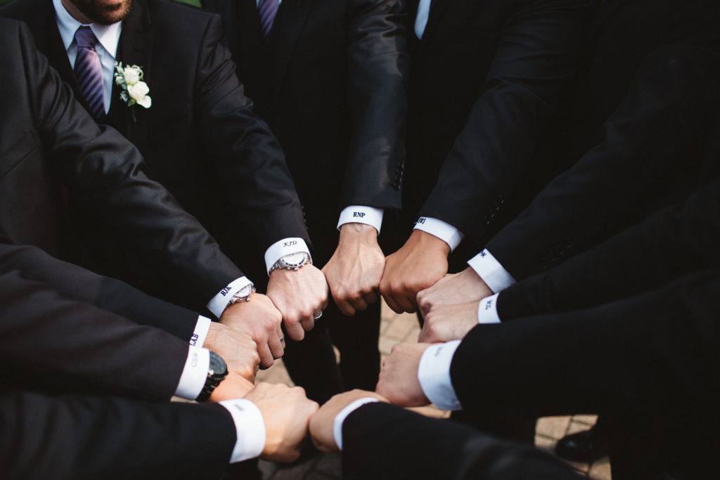 10 groomsmen hands in a circle showing off embroidered cuffs on custom suits
