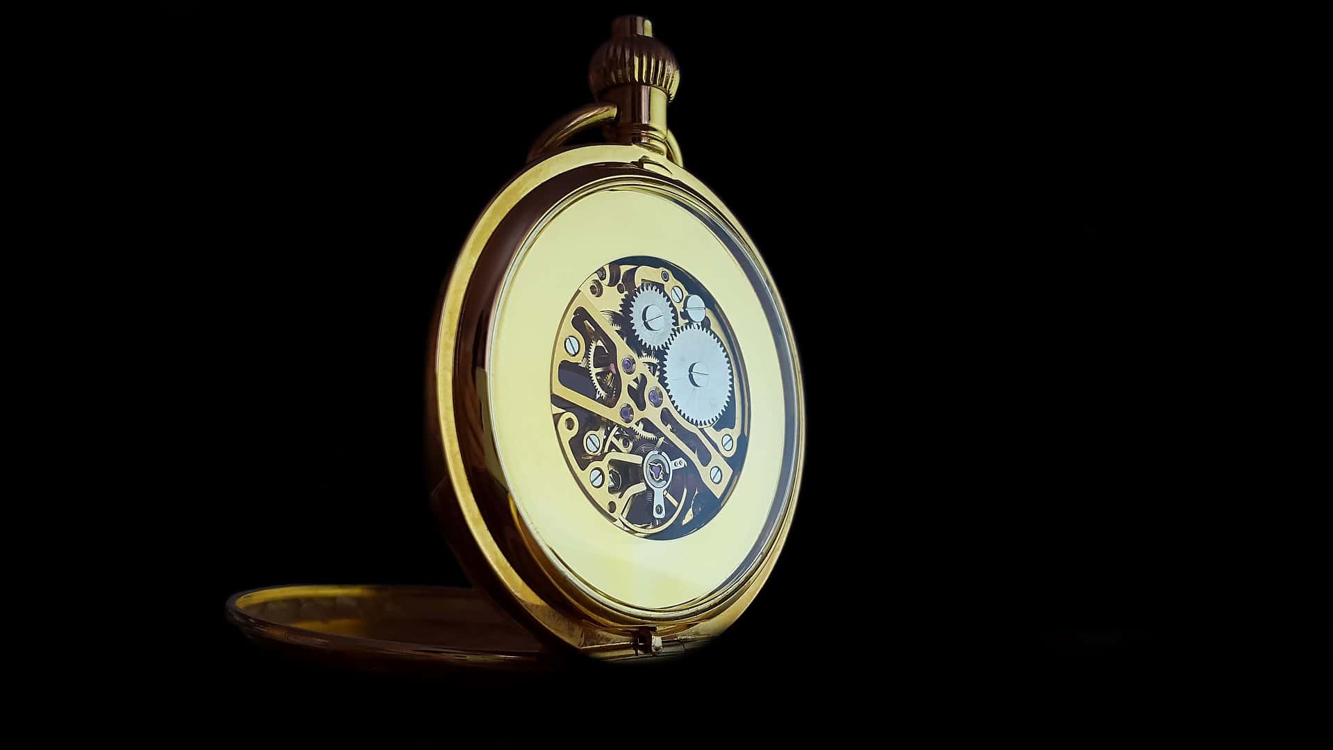 Gold colored classic pocket watch against dark black background. Internal watch components are visible.