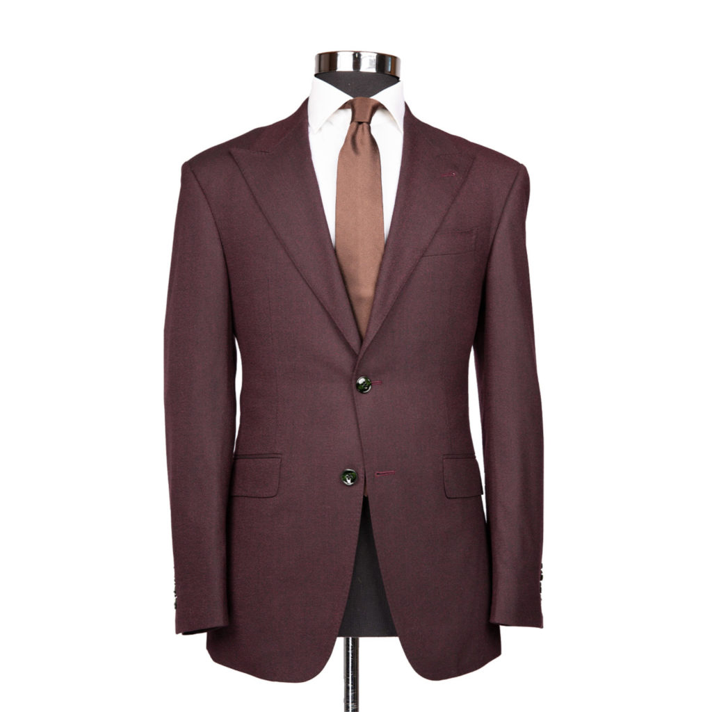 A burgundy colored suit jacket on a body form with a white shirt and mauve tie on a white background