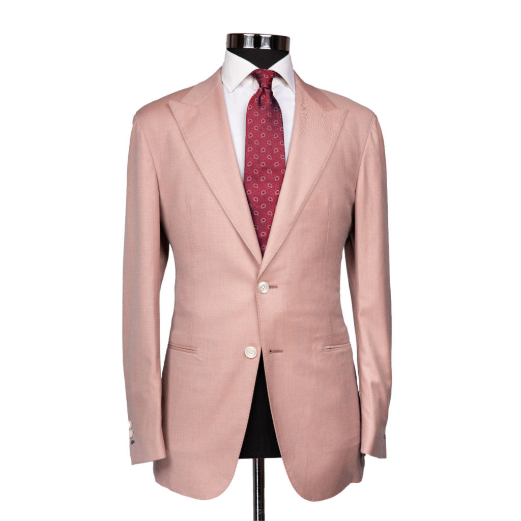 a dusty pink suit jacket on a body form with a white shirt and a maroon patterned tie on a white background