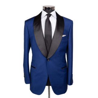 A cobalt blue tuxedo style suit jacket with black shawl lapel on a body form with a white shirt and a black tie on a white background