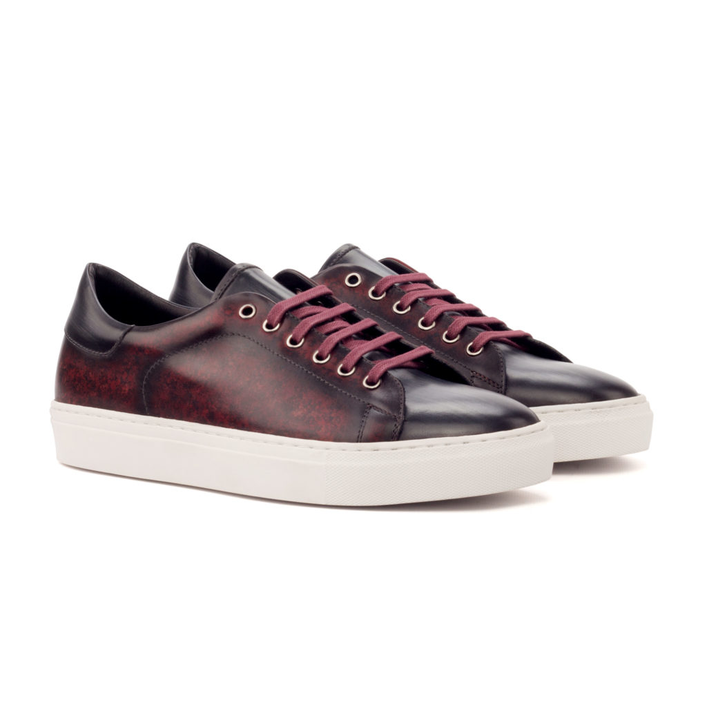 The Plimsoll: Burgundy Patina. Burgundy patina and grey patina lace up trainer style shoes with white soles on a white background