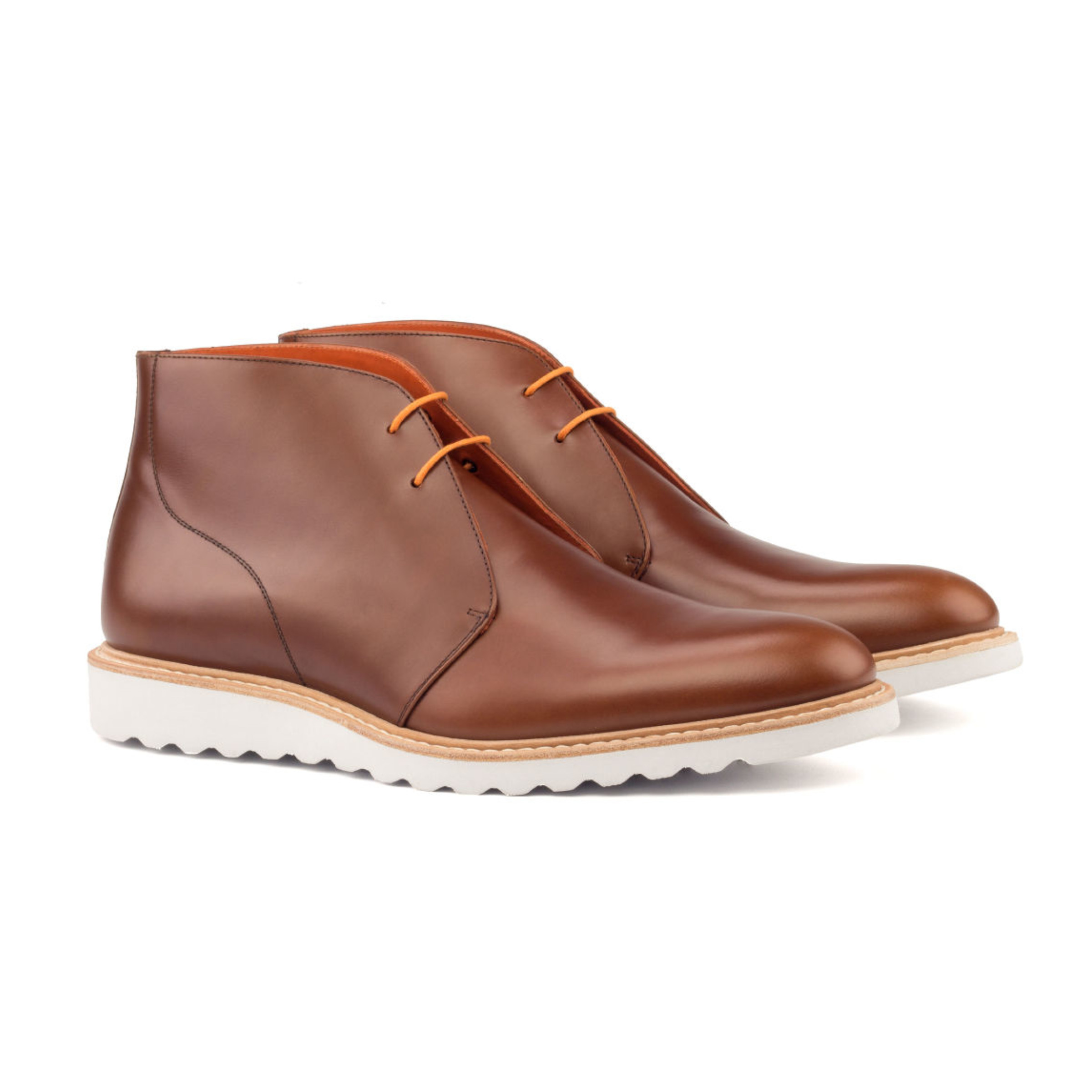 The Arborist: Polished Cognac. Front side facing view of cognac polished calf leather ankle style boots with orange laces and white soles on a white background