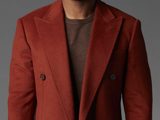 A man is wearing a red overcoat against a gray background. The image is cropped so that only the man's torso is showing.