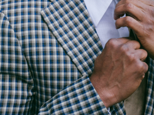 Close up view of highland checked sports jacket with notched lapel. A man's hands are tightening a tie.