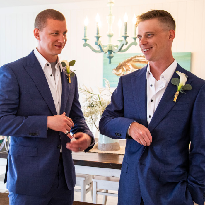 Two men are wearing matching blue suits. They are smiling and looking away from the camera.