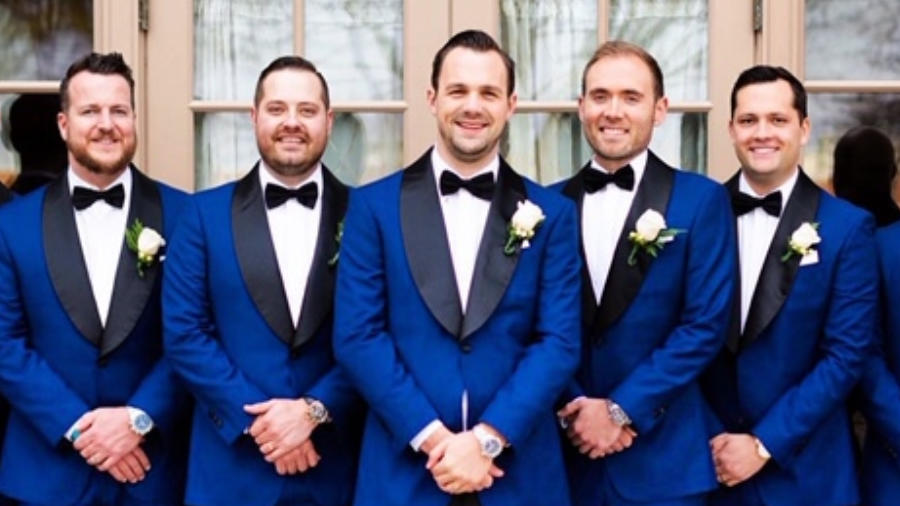 Five men wearing matching blue tuxedos smile towards the camera.